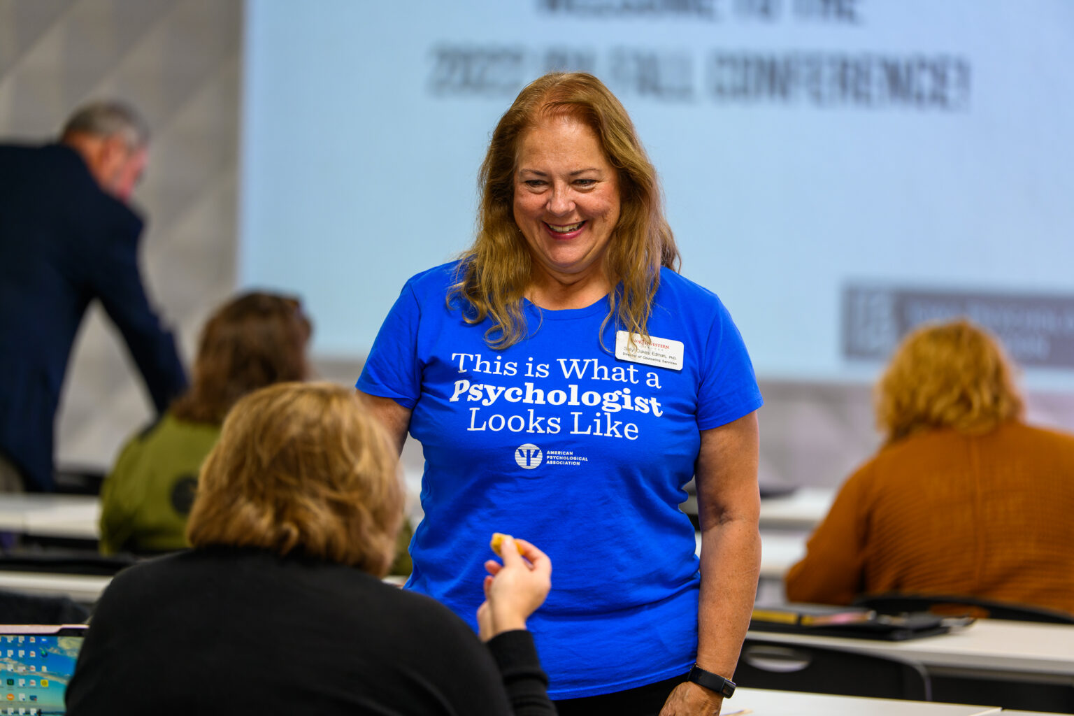 Smiling member at a conference wearing a This is What a Psychologist Looks Like' t-shirt.